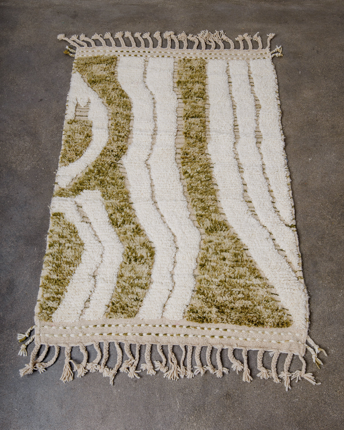 Berberlin Beniourain rug in cream and speckled khaki green, laying on concrete floor.